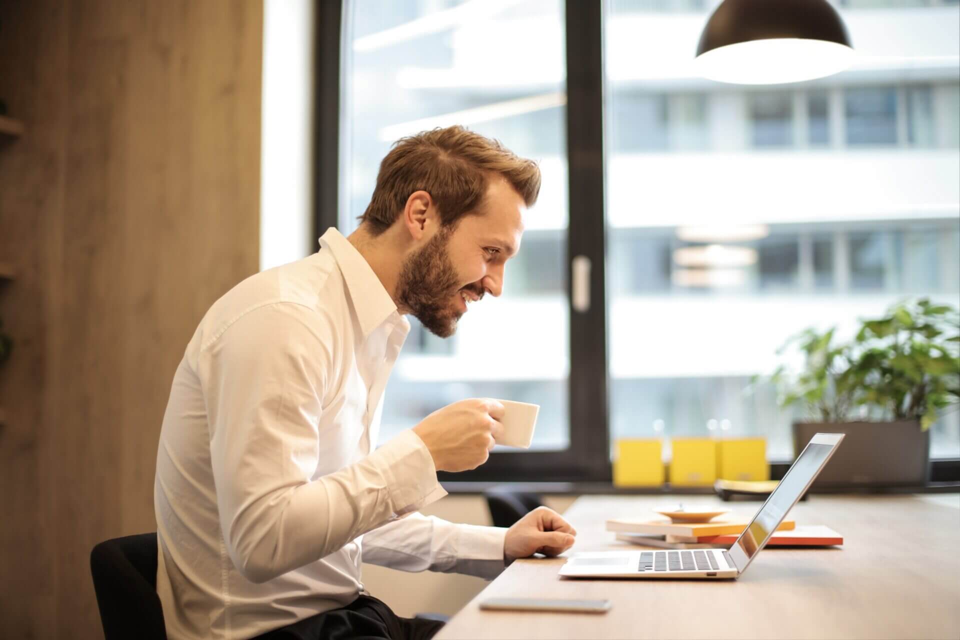 Man sitting at desk with laptop and cup of coffee, working.